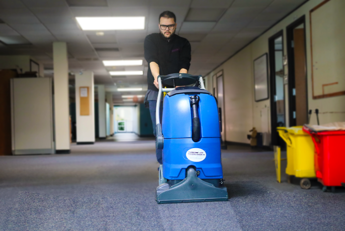 Commercial carpet cleaning technician using professional floor machine in office hallway, part of Transcend Maintenance janitorial services.