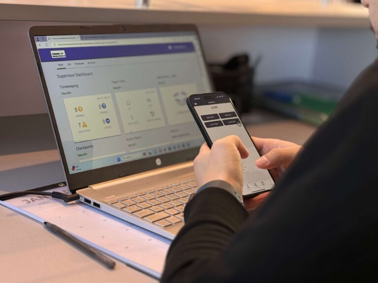 Employee accessing a supervisor dashboard on a laptop while using a mobile app for timekeeping and workforce management.