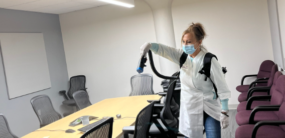 Commercial cleaner disinfecting an office conference room with electrostatic sprayer, part of Transcend Maintenance sanitization services.