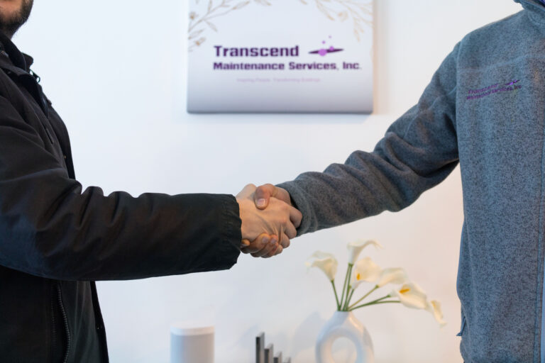 Two professionals shaking hands in front of the Transcend Maintenance Services sign, symbolizing reliable commercial cleaning partnerships.