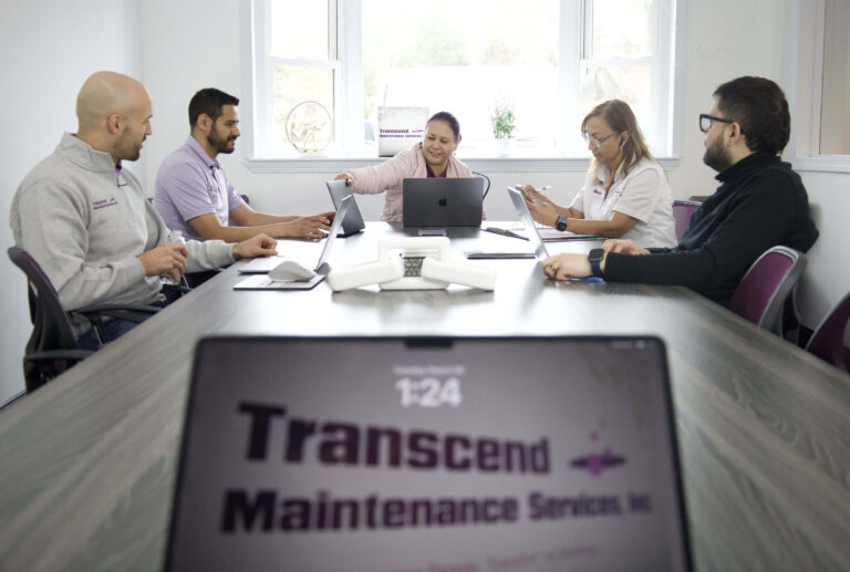 Leadership team at Transcend Maintenance Services collaborating during a strategy meeting with laptops and digital tools.