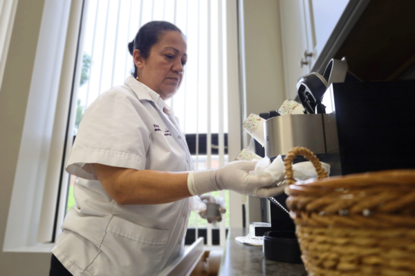 A Transcend Maintenance Services team member wearing gloves and uniform carefully restocking and cleaning a breakroom coffee station.