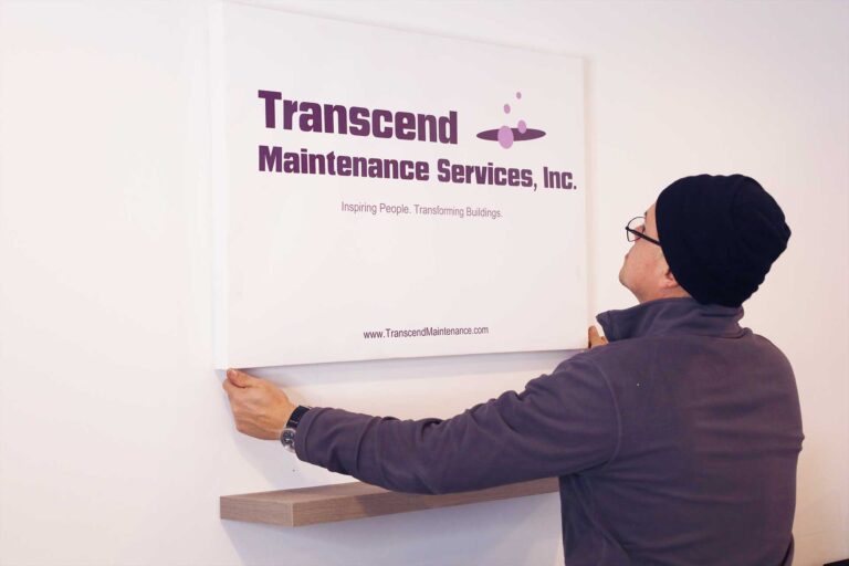 A professional installs a Transcend Maintenance Services sign on the wall, showcasing the company’s brand and commitment to excellence.