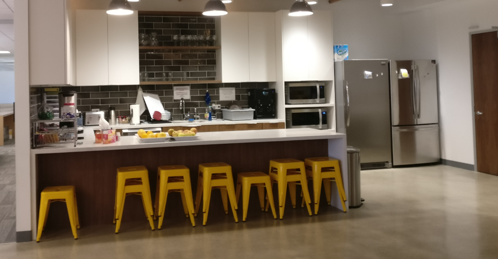 Clean and well-maintained office kitchen with stainless steel appliances, white cabinets, and yellow stools, showcasing professional commercial cleaning services.